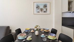 En spiseplads med et bord dækket til fire personer, komplet med mønstrede skåle, en vase med blomster og et indrammet billede på væggen.