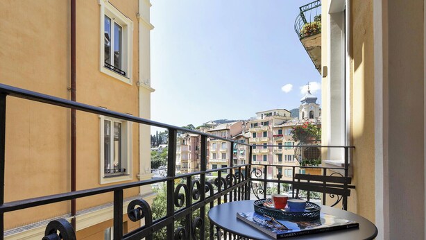En balkon med et bord og en stol, med udsigt over en by med bygninger og et tårn med et ur.
