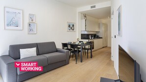 En moderne lejlighed med en grå sofa, et spisebord med stole, et køkken og billeder i rammer på væggene.