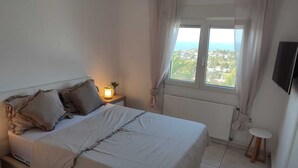 A bedroom with a bed, a bedside table with a lamp, a window with curtains, and a view of the outside. - Beautiful Villa with gorgeous seaviews, close to the centre andbeaches of Denia. (Denia)