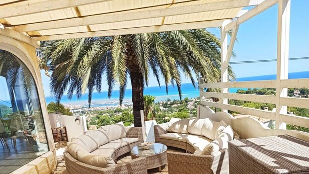 A covered outdoor seating area with wicker furniture and a glass table set for two. - Beautiful Villa with gorgeous seaviews, close to the centre andbeaches of Denia. (Denia)