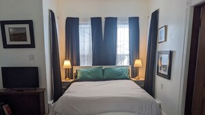 Un cuarto de hotel ordenado con una cama grande, dos lámparas de noche, un televisor sobre un soporte de madera y cuadros enmarcados en las paredes.