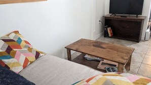 Una sala de estar con un sofá, una mesa de centro de madera, un televisor sobre un mueble bajo y una estantería.