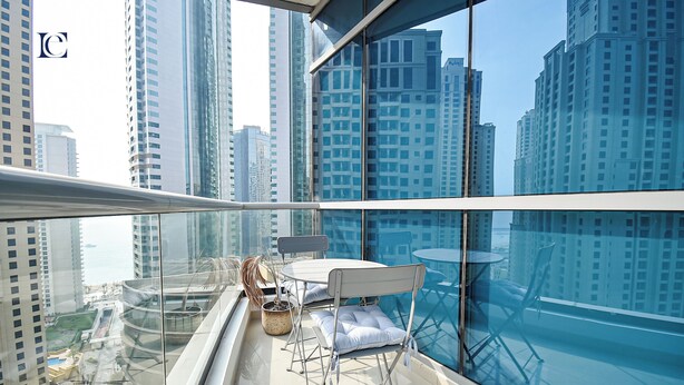 A high-rise balcony with a glass railing, a table with chairs, and a potted plant. - Brand New Studio with Marina View -PAU (Dubai)