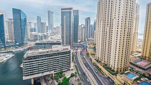 A high-rise building with a modern design, surrounded by other tall buildings, a busy road, and a body of water. - Brand New Studio with Marina View -PAU (Dubai)
