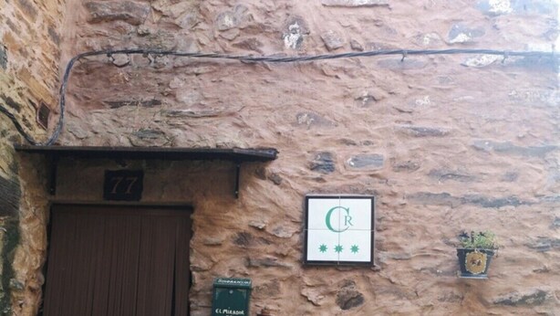Un mur de pierres rustiques avec une porte en bois portant le numéro « 77 », une horloge et des plantes en pot.