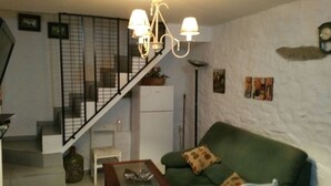 Un salon avec un canapé vert, une table basse, un escalier doté d’une rampe, un réfrigérateur blanc et un lustre.
