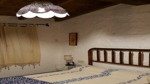 Une chambre à coucher avec une tête de lit en bois, un lit recouvert d’une couvre-lit à motifs floraux, une table de chevet avec une lampe et une fenêtre avec des rideaux.