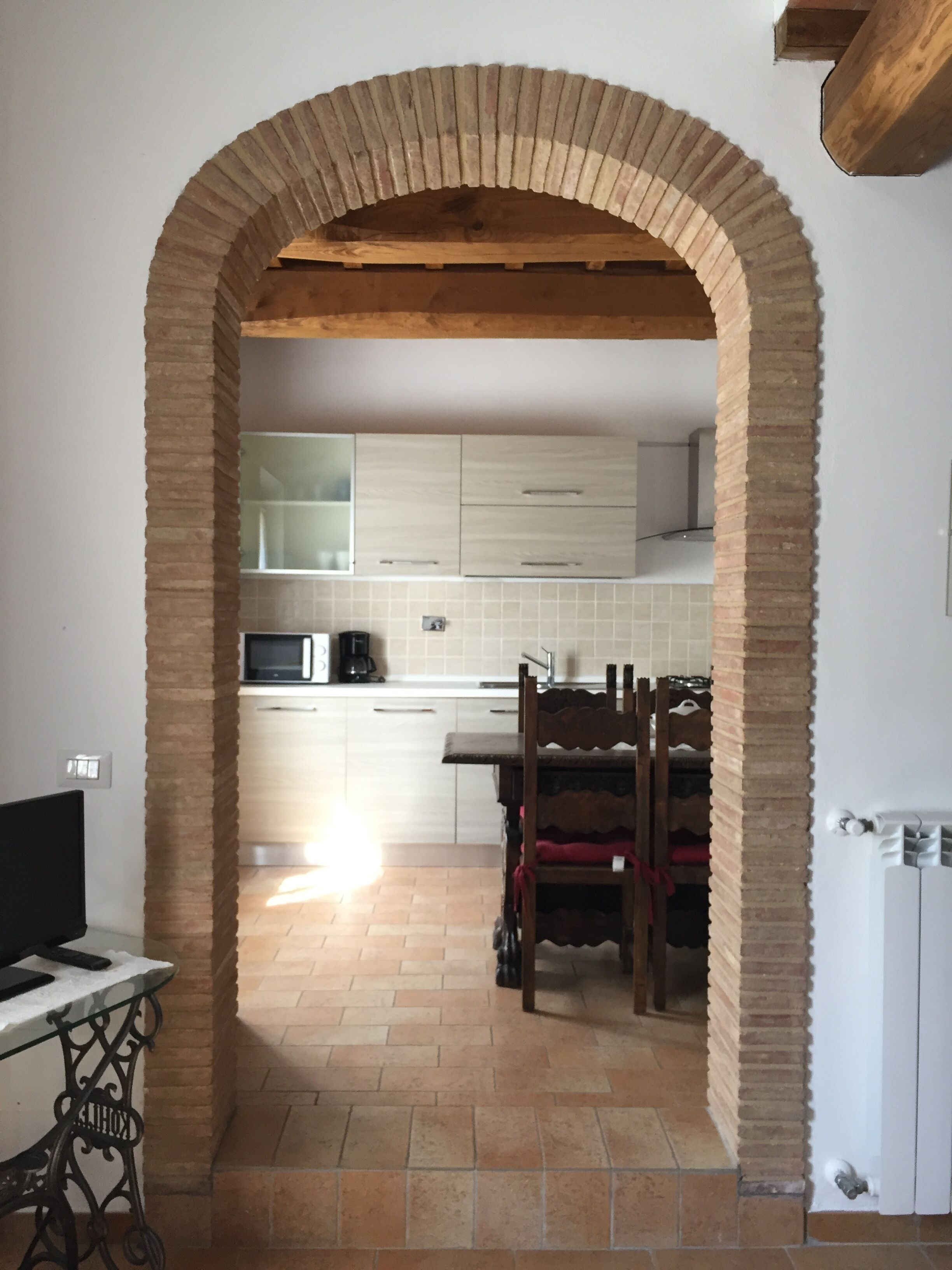 A kitchen with an arched brick entrance, white cabinets, a microwave, and a dining area with a wooden table and chairs.