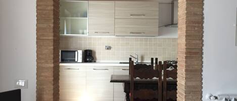A kitchen with an arched brick entrance, white cabinets, a microwave, and a dining area with a wooden table and chairs.