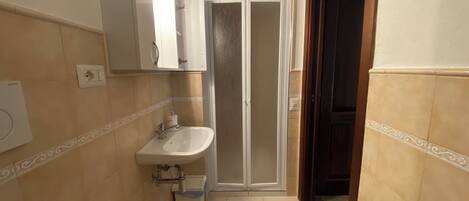 Une petite salle de bain avec un lavabo blanc, un miroir et une porte de douche.