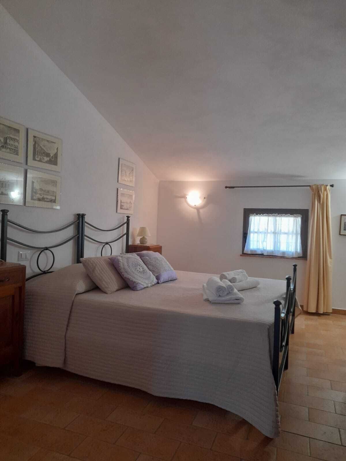 A bedroom with a bed, a nightstand, a lamp, and a window with curtains.