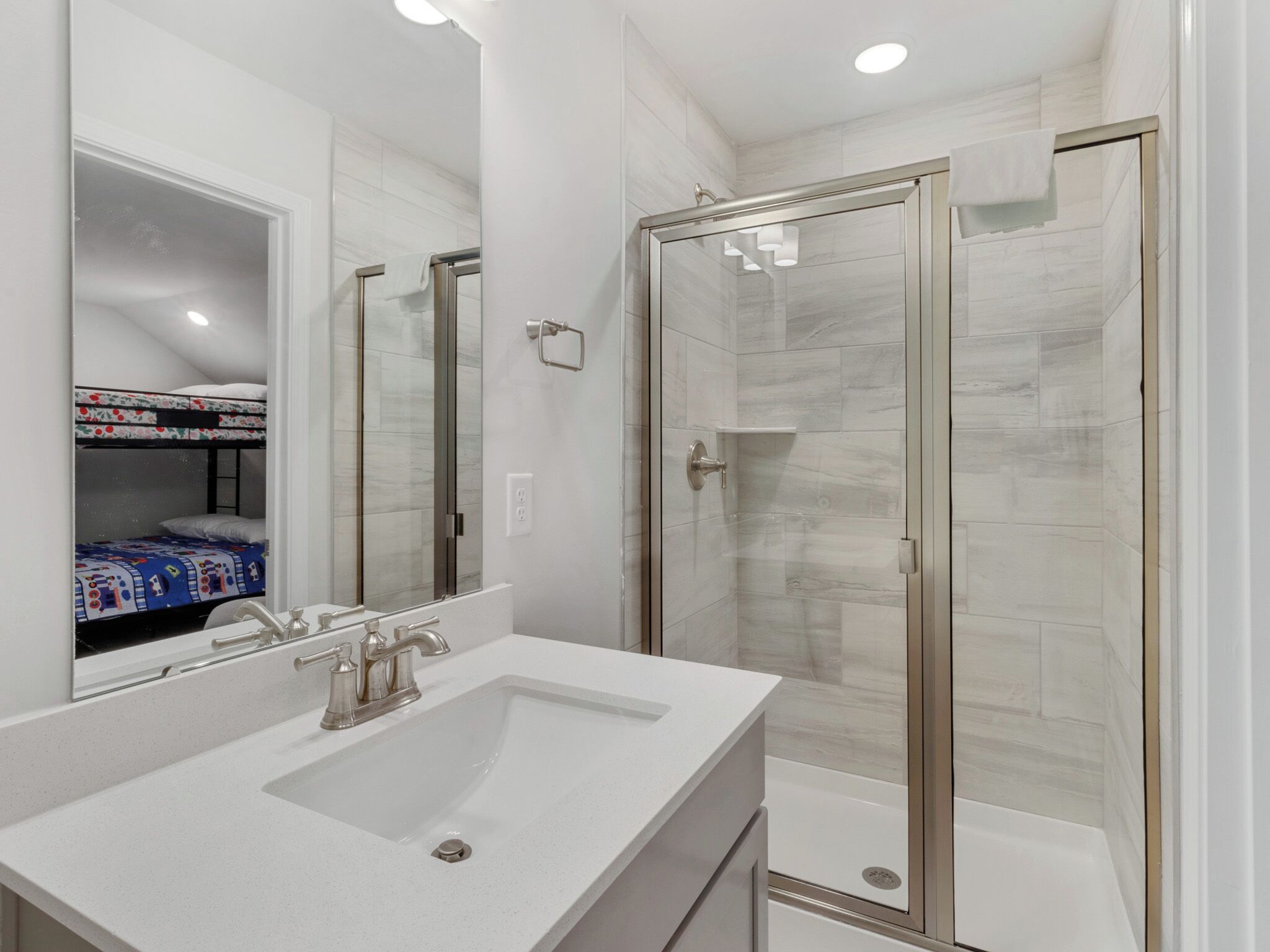 A modern bathroom with a large mirror, a white sink, and a glass-enclosed shower.
