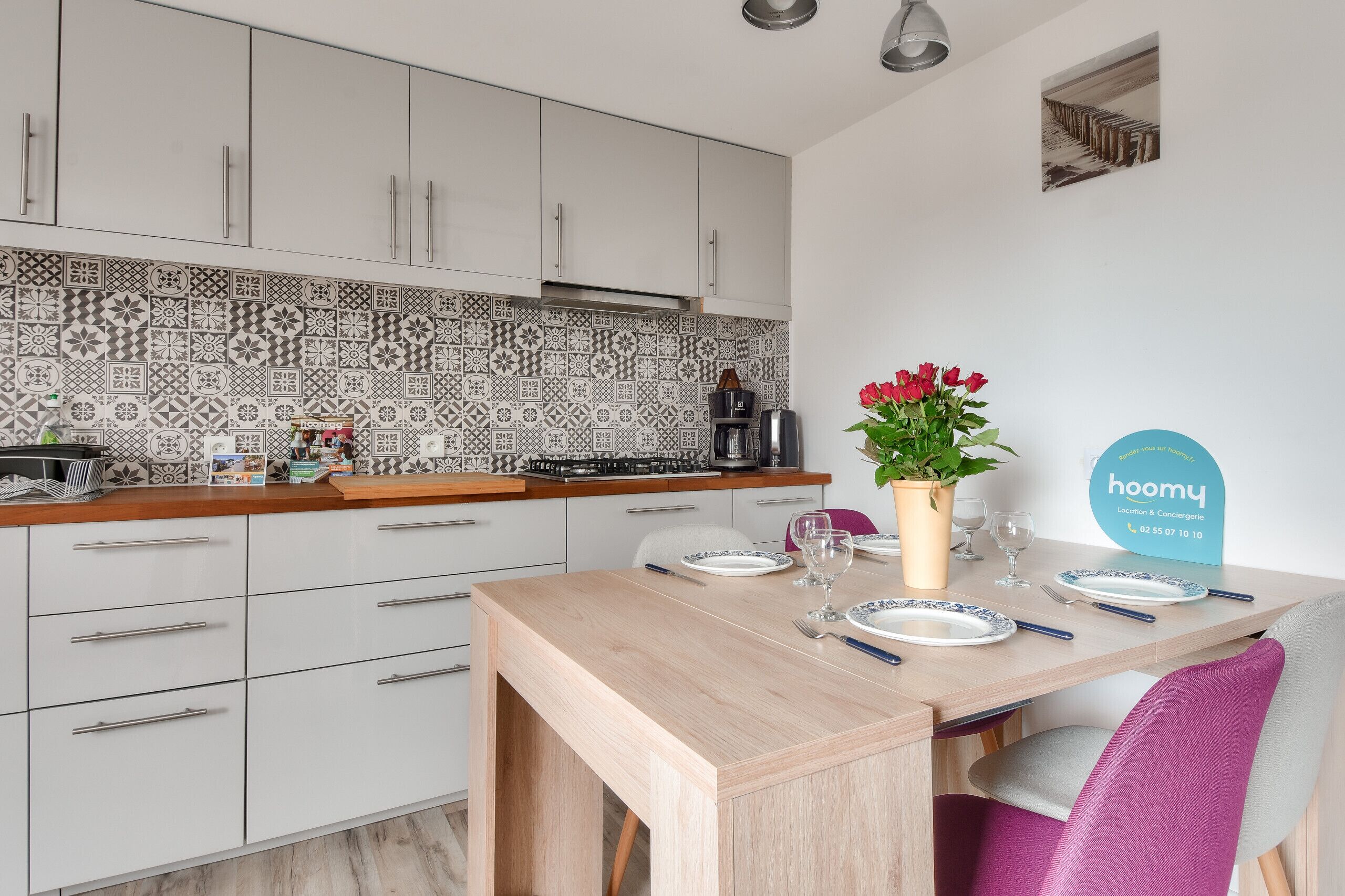 Et moderne køkken med lyse skabe, et mønstret backsplash og et spiseområde med et bord dækket til to.