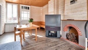 A cozy cabin interior with a wooden dining table, chairs, a sofa, a fireplace, and a television.