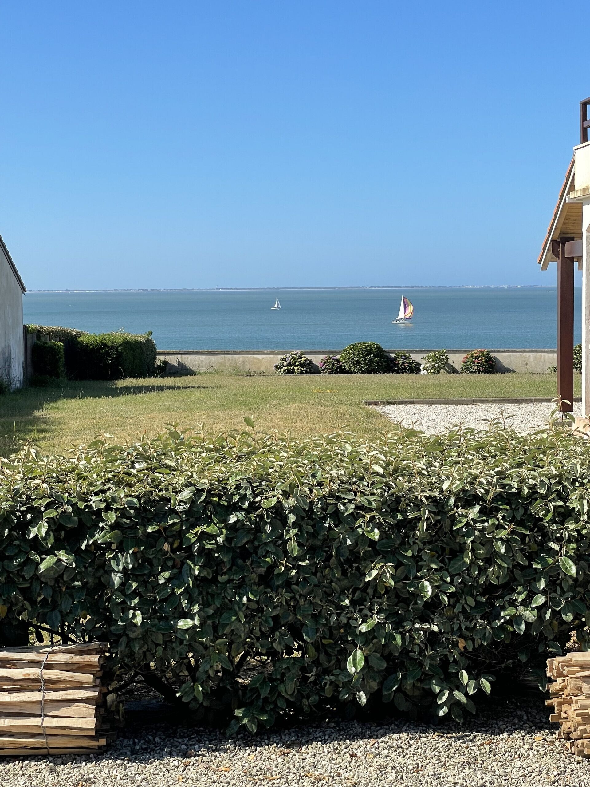 A coastal view with a grassy area, a hedge, and a building with a sloped roof.