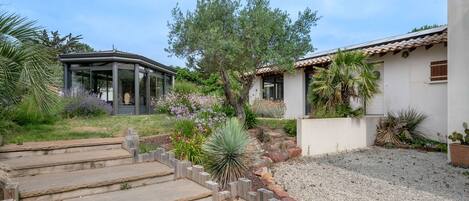 A modern house with a patio, a covered outdoor area, and a garden with various plants and flowers.