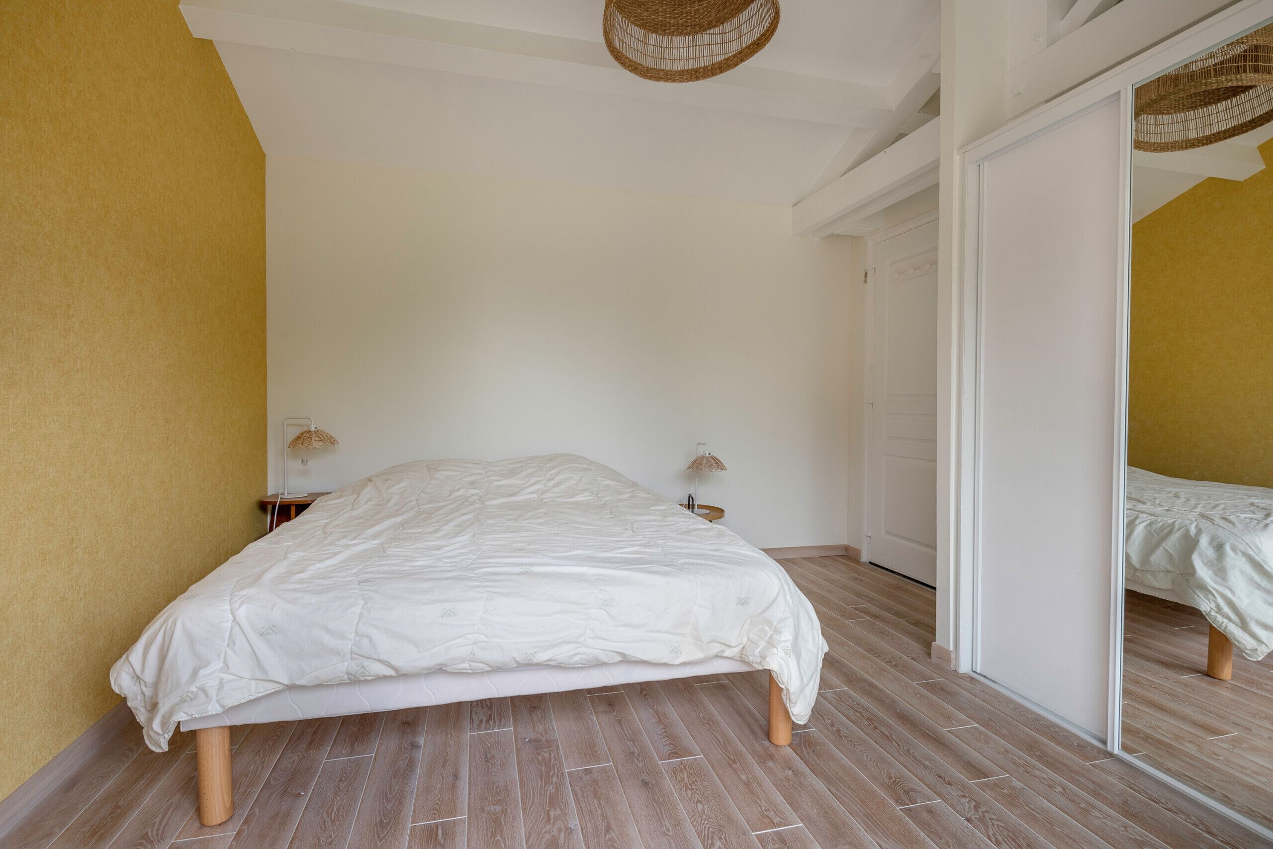 Un dormitorio con una cama grande, suelo de madera, techo blanco y pared amarilla.