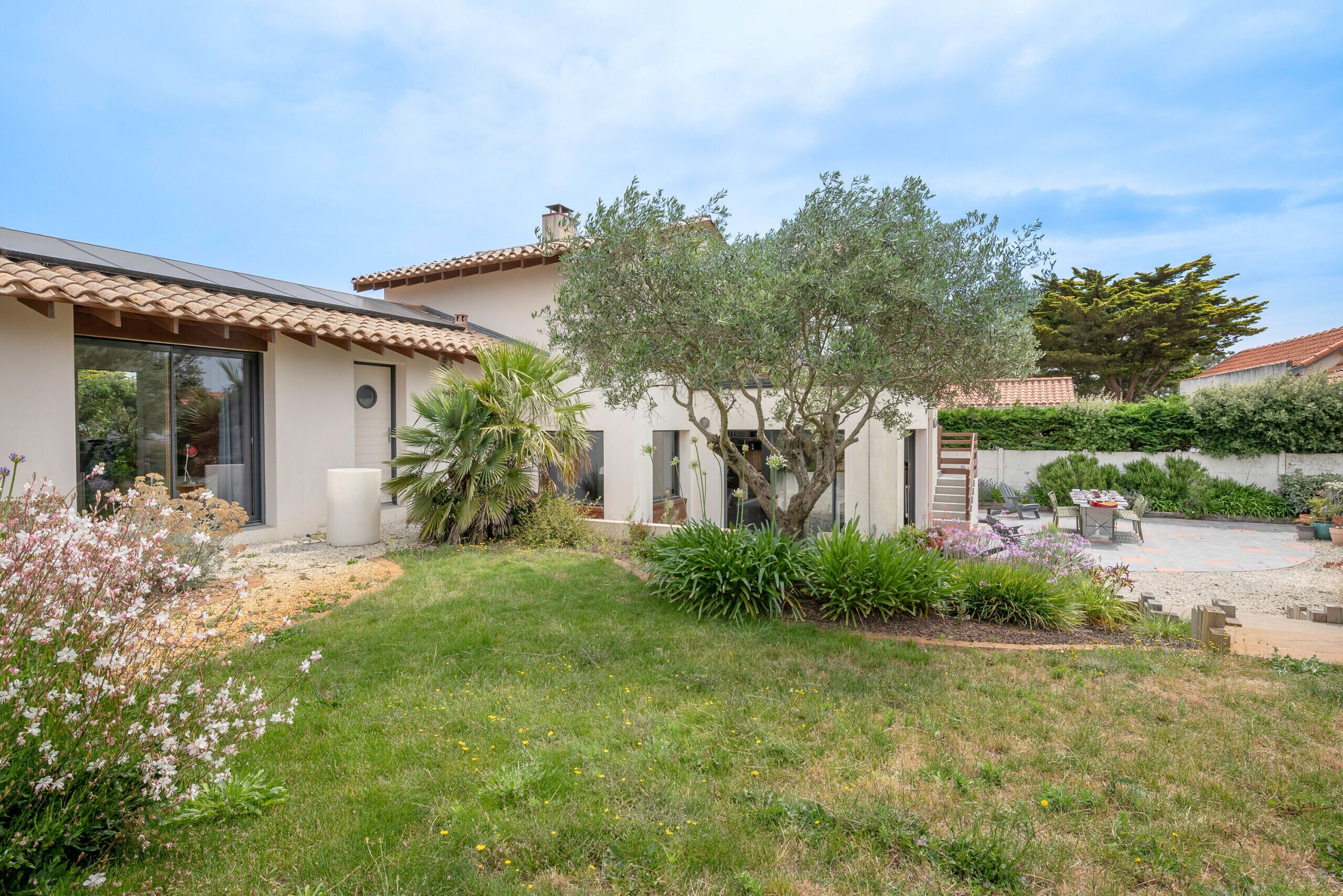 A house with a tiled roof, a patio with a table and chairs, and a garden with various plants and flowers.
