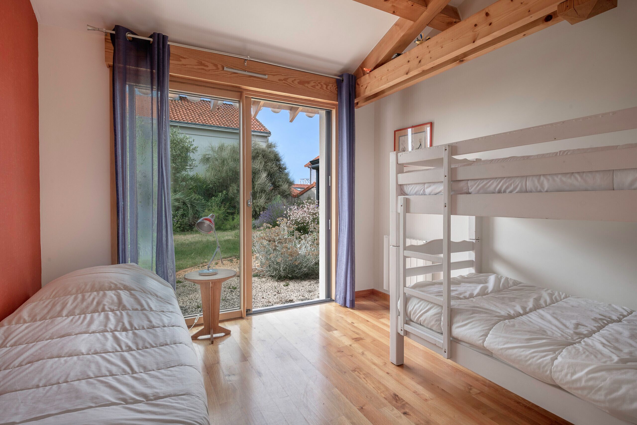 Une chambre avec deux lits, une petite table et une porte-fenêtre coulissante donnant sur un jardin.