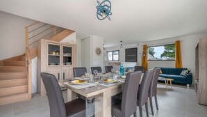 A dining area with a wooden table and chairs, a staircase, a kitchen, and a living area with a sofa. - Tour-du Parc - Modern house for 8 (Le Tour-du-Parc)