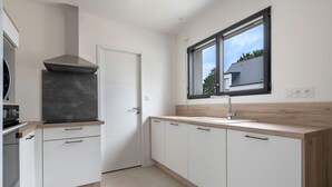A modern kitchen with white cabinetry, a built-in stove, and a window with a view of the outside. - Tour-du Parc - Modern house for 8 (Le Tour-du-Parc)