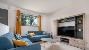 A modern living room with a blue sofa, a coffee table, and a TV stand with shelves. - Tour-du Parc - Modern house for 8 (Le Tour-du-Parc)