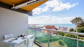 A balcony with a table and chairs, overlooking a coastal view with buildings and greenery. - Holiday with sea view in Pléneuf-Val-André (Pléneuf-Val-André)
