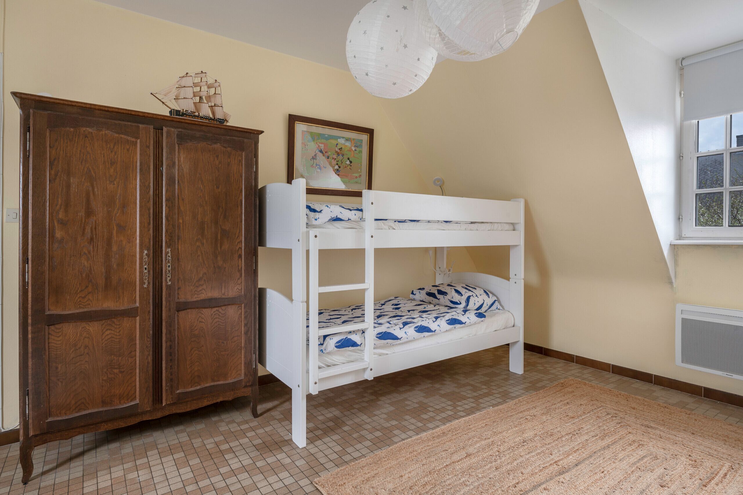Een kamer met een stapelbed, een houten garderobe en een raam met uitzicht.