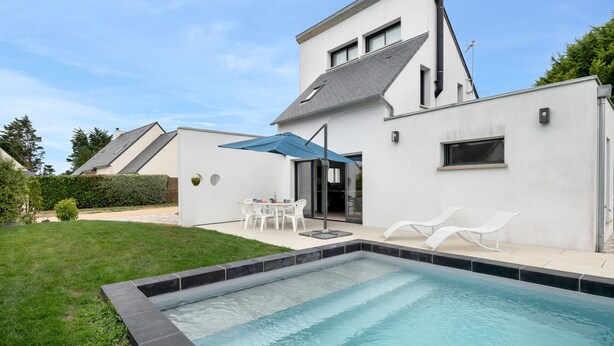 Una casa moderna con piscina, un patio con mobiliario exterior y un césped bien cuidado.