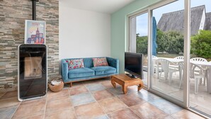 Una sala de estar con pared de piedra, un sofá azul, un televisor y un ventanal corredizo a un patio exterior.
