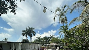 An outdoor dining area with white tables and gold-rimmed plates, set against a backdrop of a swimming pool and palm trees. - Private Pool, Gazebo, Firepit, and Hot Tub. Optional Guest Suite (Lake Worth)