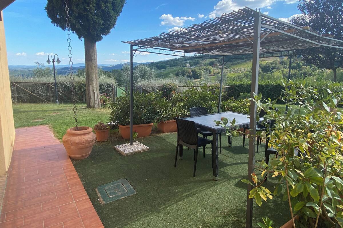 A patio with a table and chairs, surrounded by potted plants and a pergola.