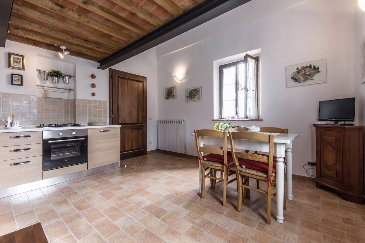 A kitchen with a wooden ceiling, a dining table with chairs, a stove, and a radiator.