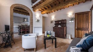 A spacious living area with a high ceiling, a fireplace, a dining area, and a kitchen visible through an archway. - Villa Le Ripe Apartments (Gambassi Terme)