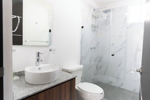 Et moderne badeværelse med en rund vask, toilet og brusekabine med glasvægge.