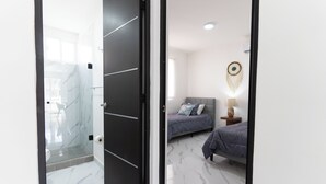 Une chambre moderne avec une douche en verre, un lit avec une tête de lit et une table de chevet avec une lampe.