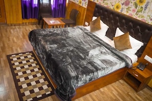 A bedroom with a large bed, a wooden headboard, a bedside table with a phone, and a checkered rug. - Hotel HONEY N SPICE (Dharamshala)