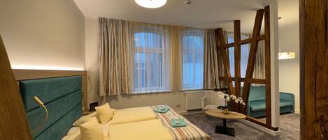 A hotel room with a bed, a wooden ladder, a small table with a vase, and a window with curtains.