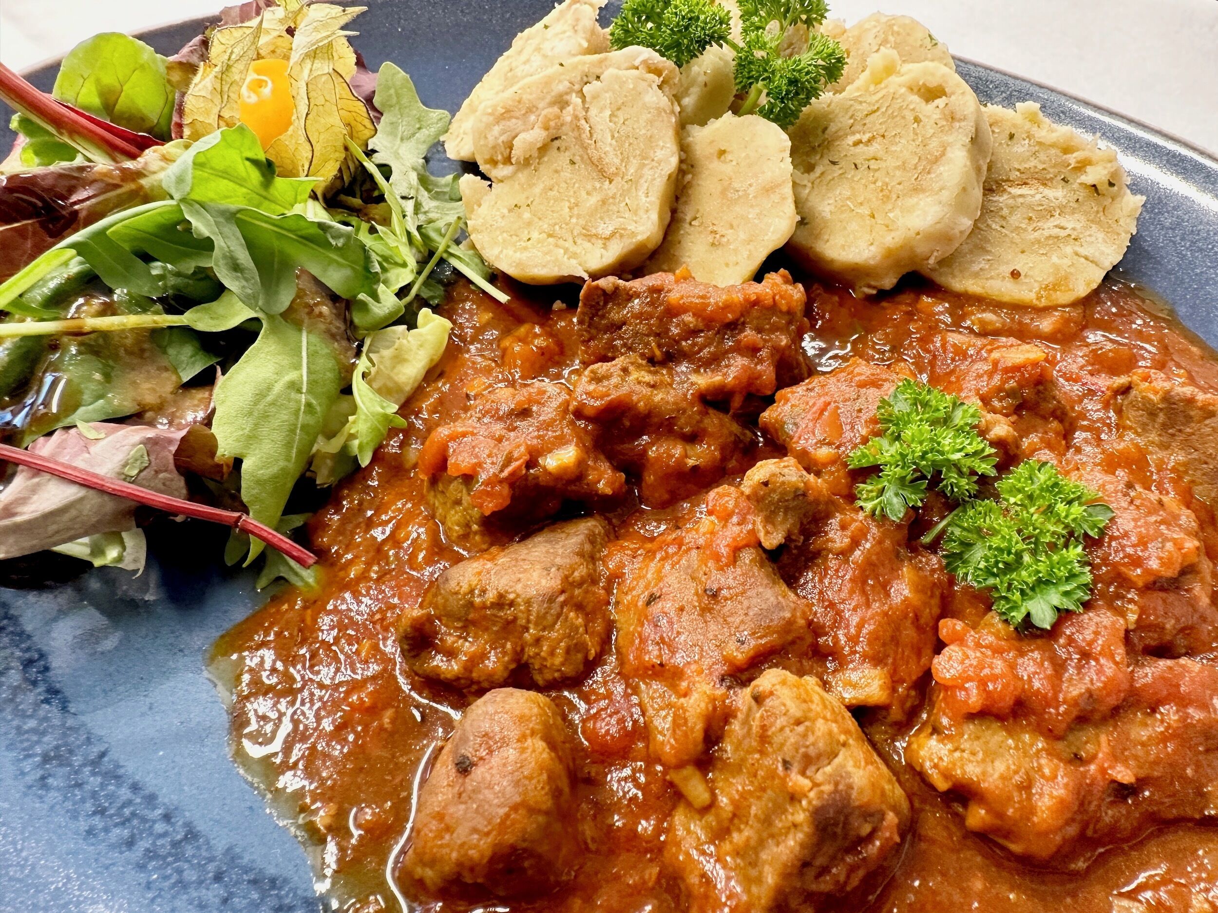 A plate of meatballs in tomato sauce, accompanied by boiled potatoes and a side salad.