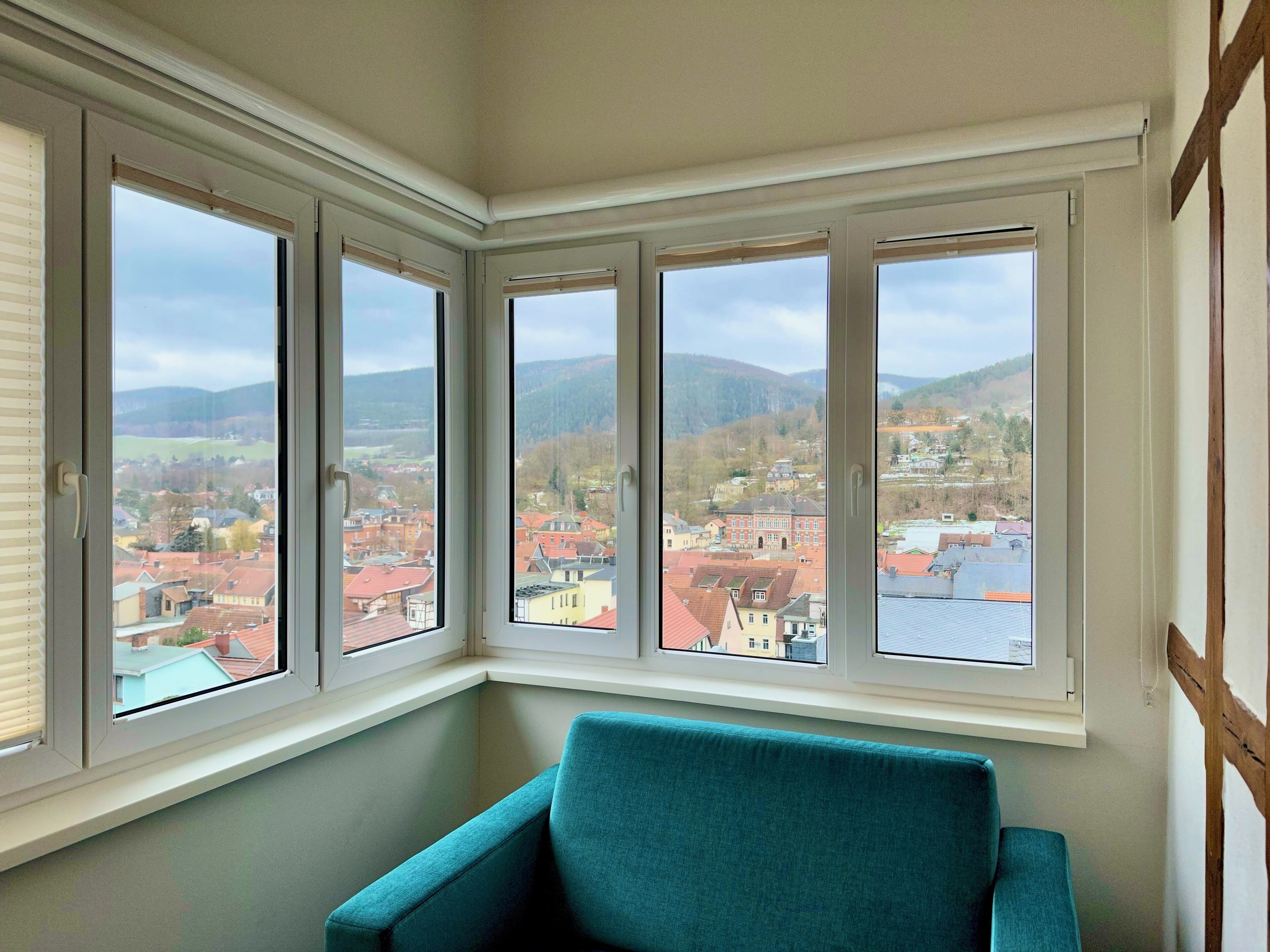 A corner room with a large bay window overlooking a town and hills.