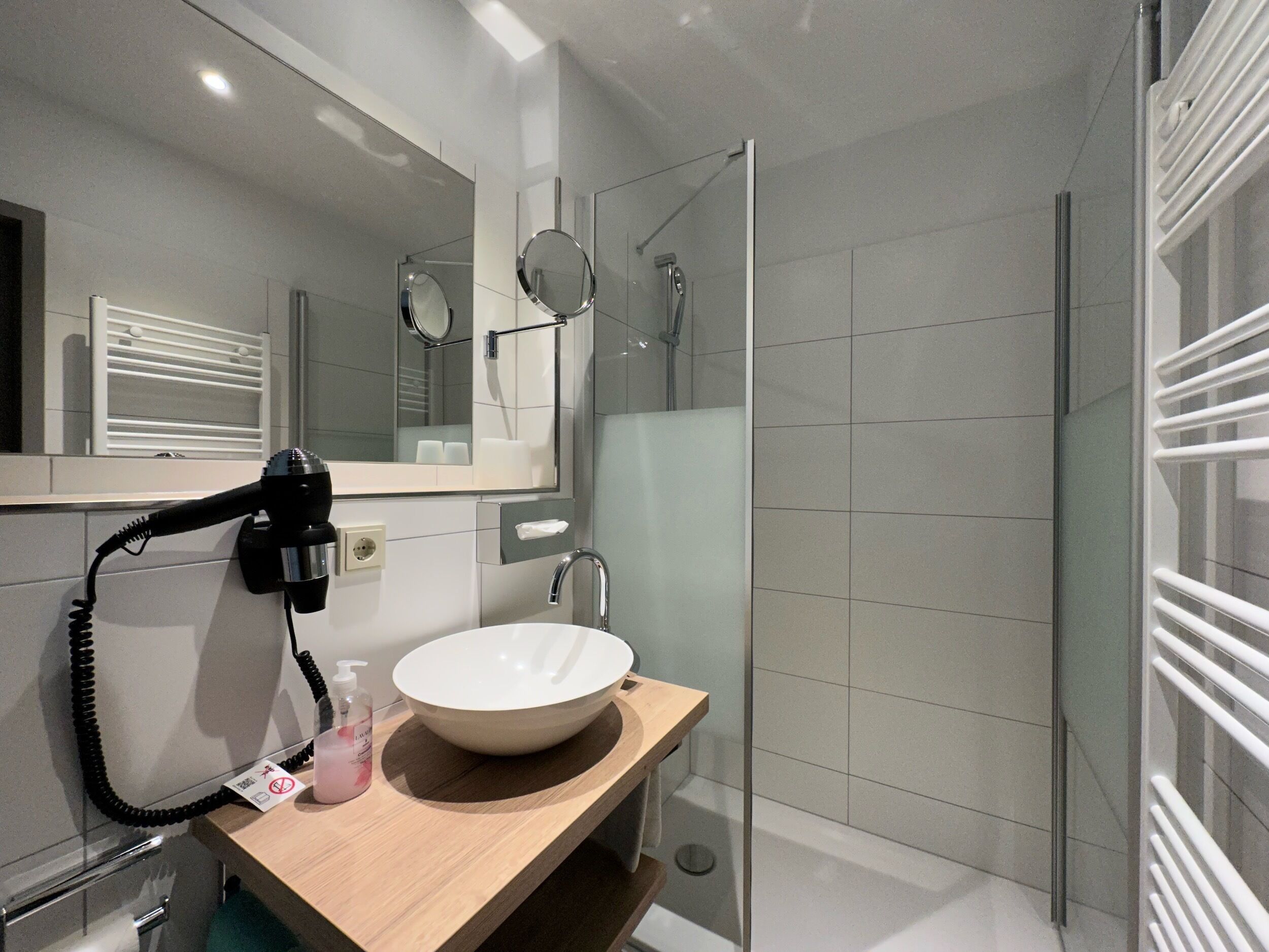 Un baño moderno con un lavamanos blanco, un secador de pelo y una cabina de ducha de vidrio.