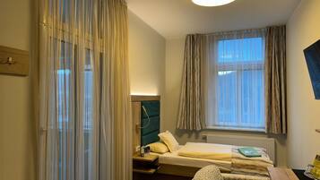 A hotel room with a bed, a desk, a chair, a window with curtains, a headboard, and a ceiling light.