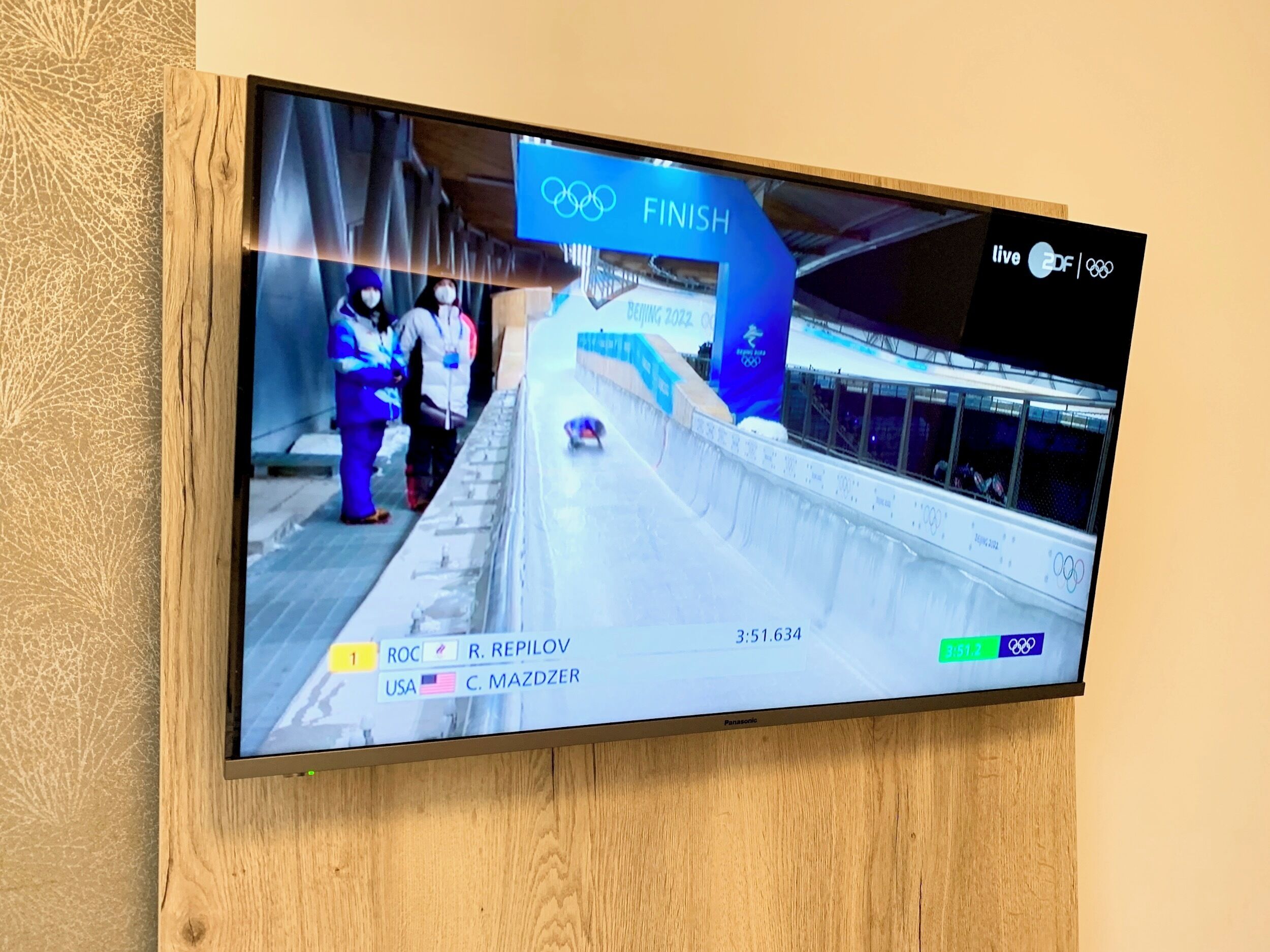 A television displaying a finish screen of a bobsled race with the Olympic rings logo and the word "FINISH" prominently displayed.