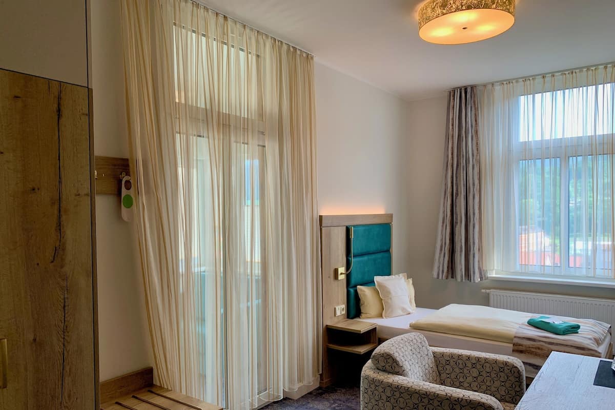 Una habitación de hotel con cama, escritorio, silla y ventana con cortinas.
