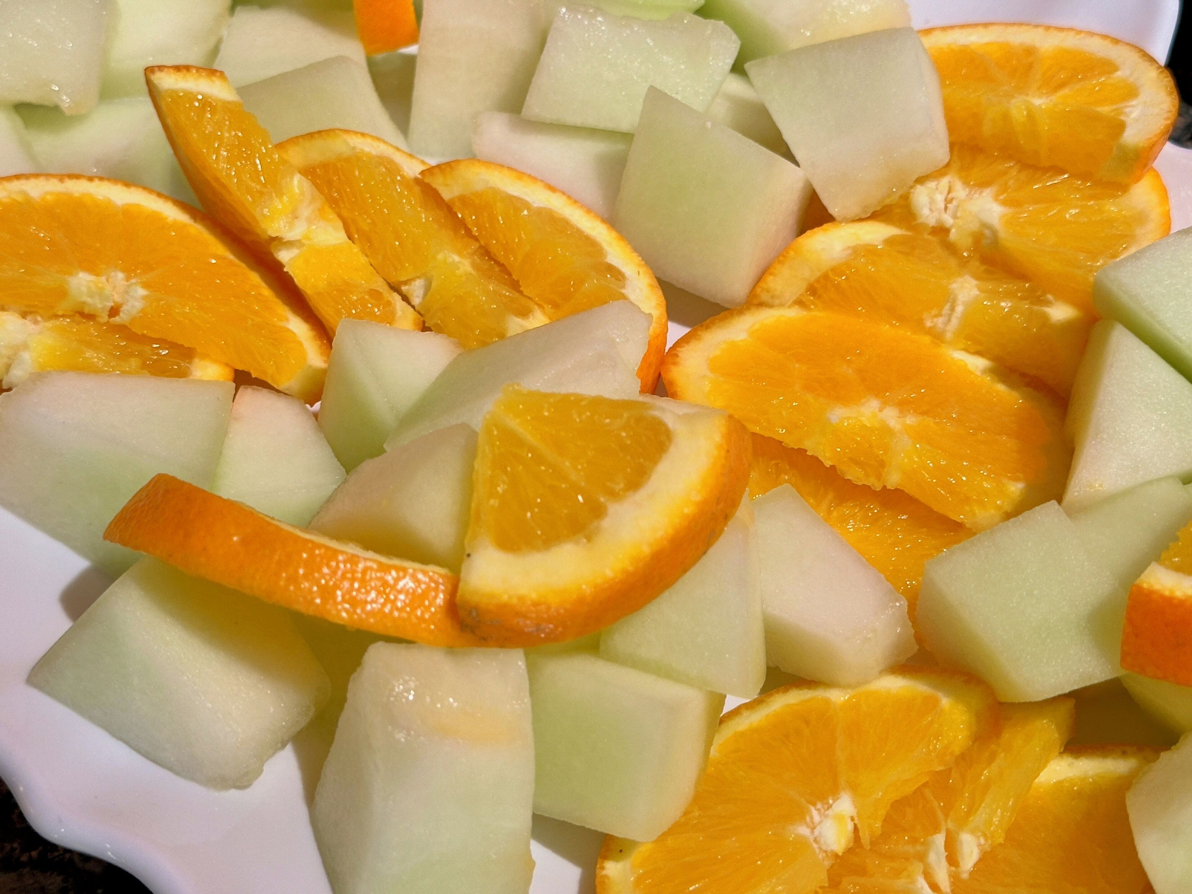 A plate of fruit consisting of orange slices and melon pieces.