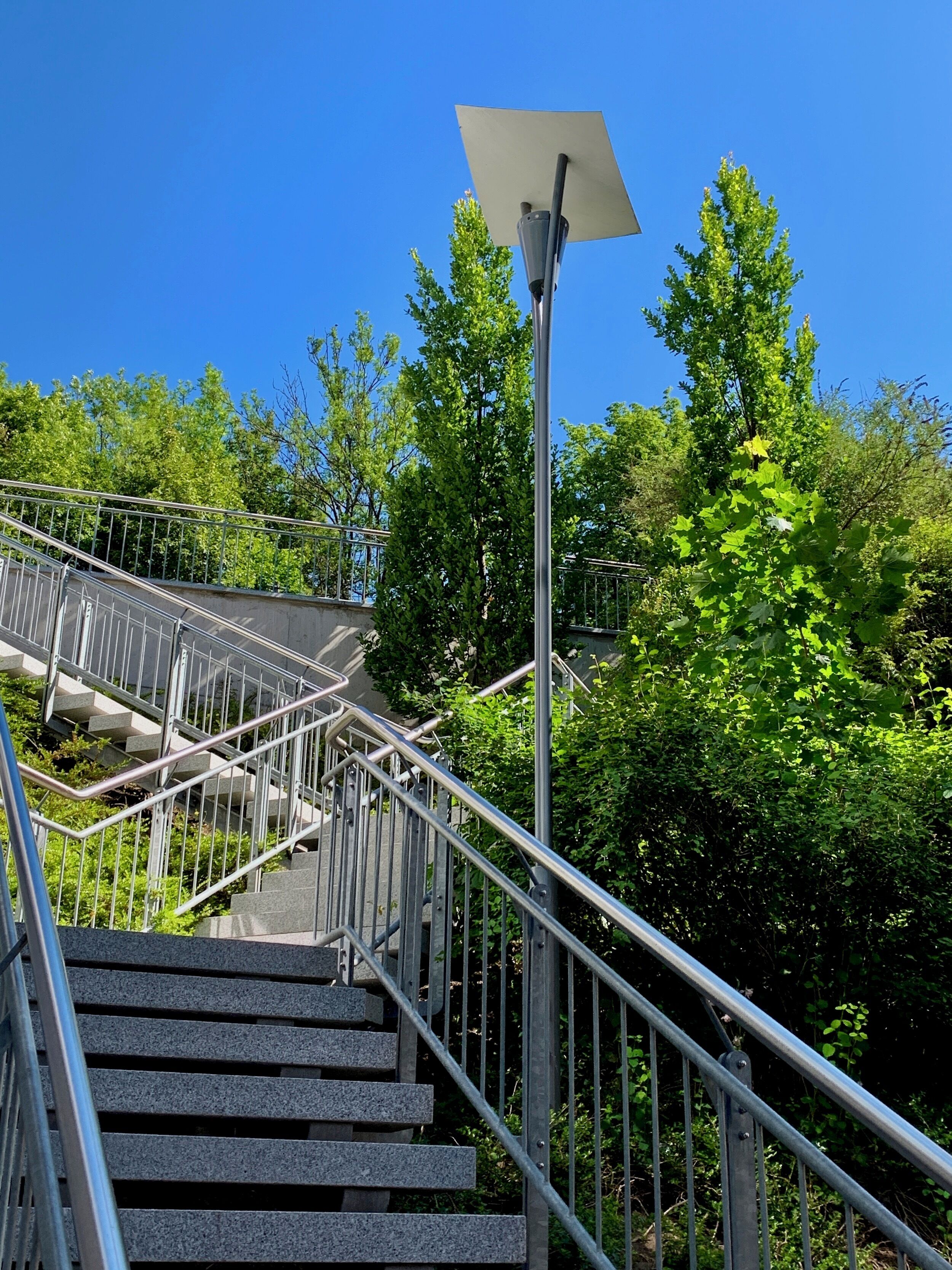 Un escalier avec des rampes en métal et un panneau solaire fixé sur un poteau.