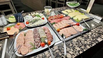 Una mesa de bufé con diversos alimentos, como carnes, quesos y verduras, dispuestos en platos y bandejas.
