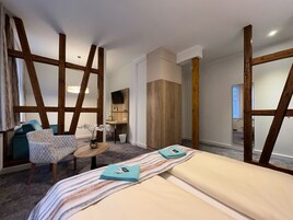 Quarto de hotel com uma cama, uma cadeira, uma mesinha e uma televisão.