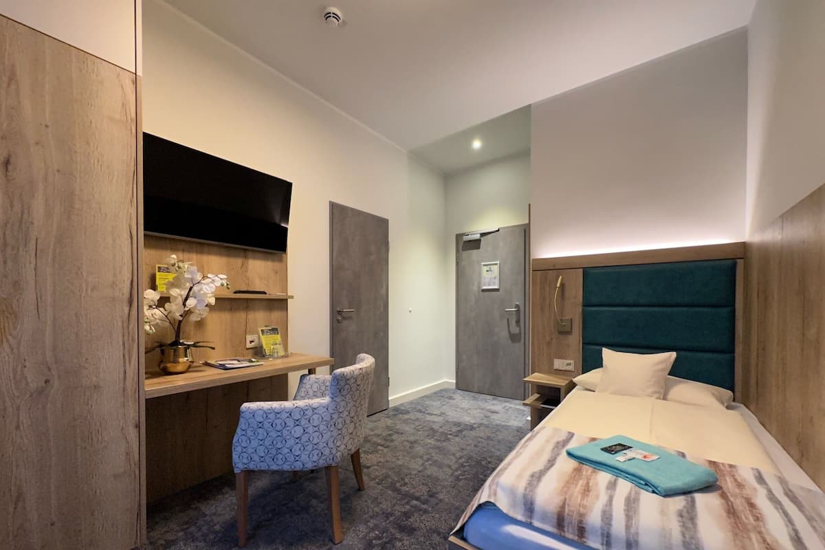Una habitación de hotel moderna con una cama, un escritorio, una silla, un televisor y un armario.